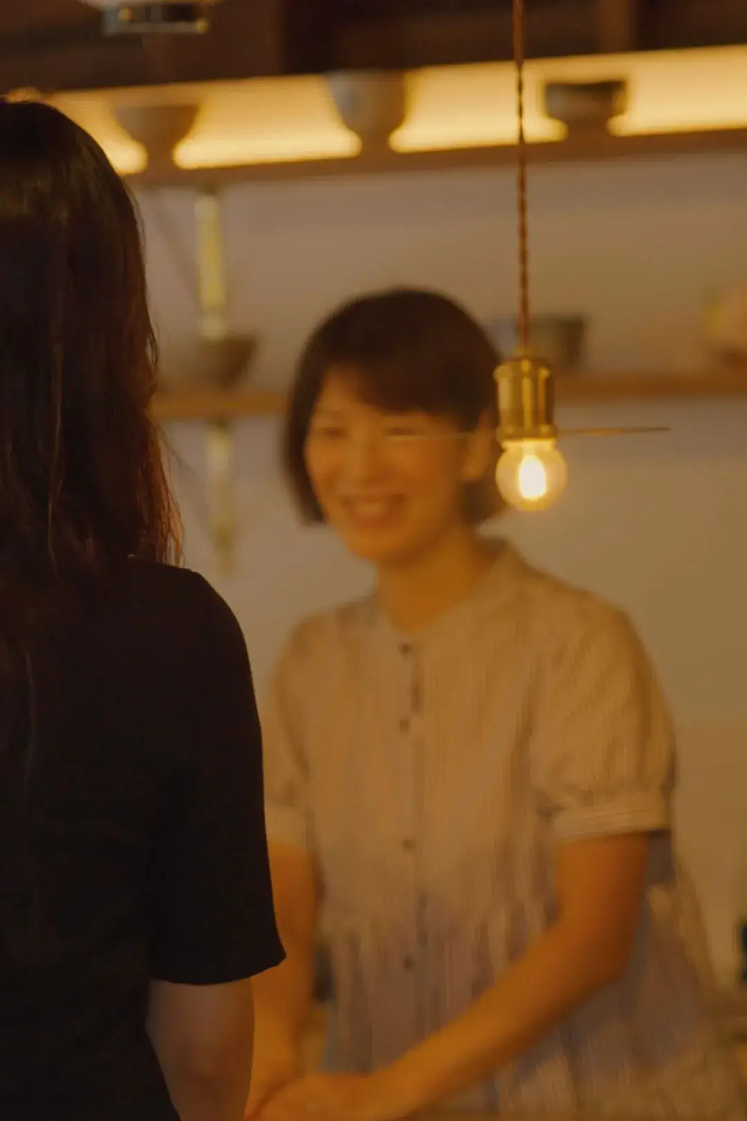 器の並ぶ店で、店の人と向き合って話す女性の後ろ姿