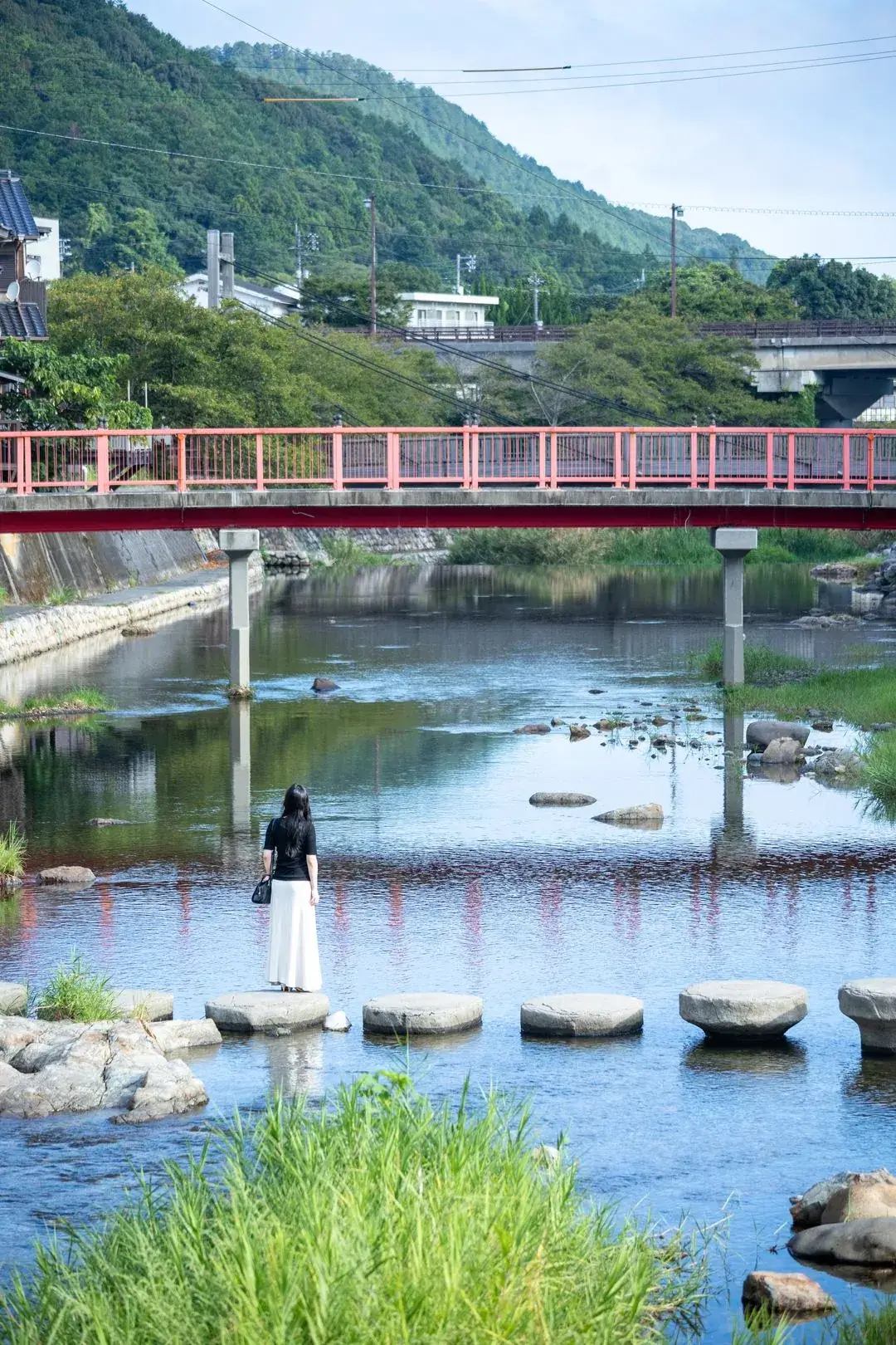音信川の飛び石に立つ女性と赤い橋