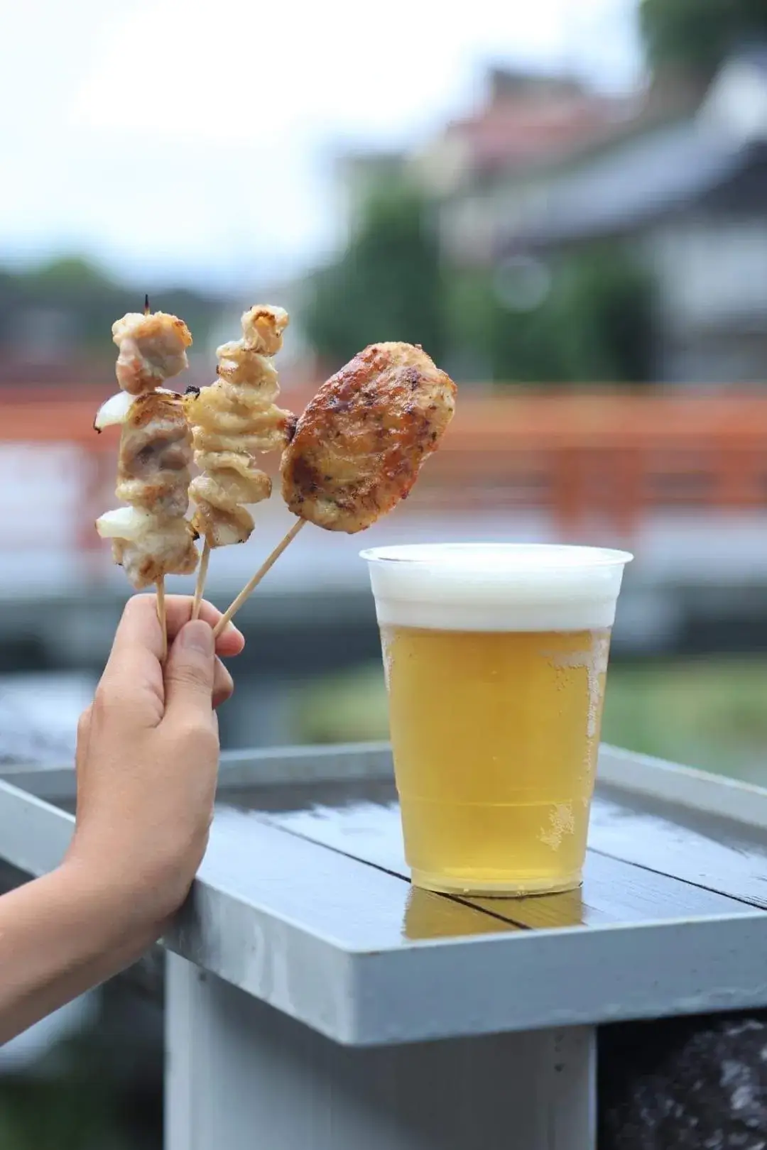 音信川沿いで焼き鳥の串と生ビールを手にする