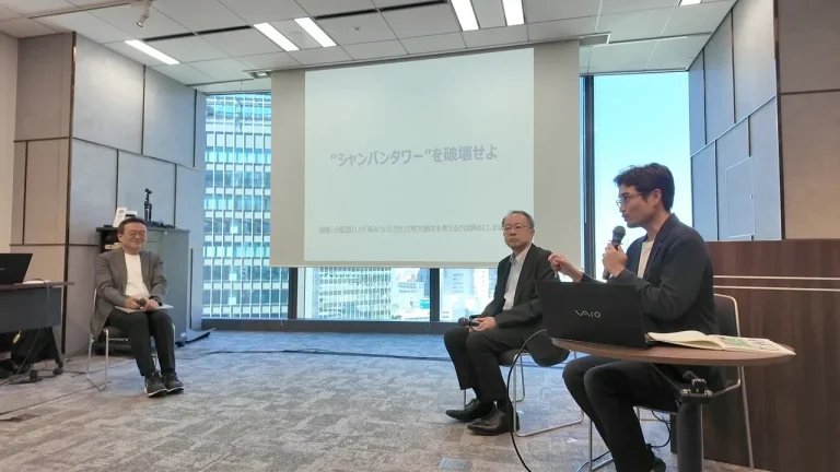 「“シャンパンタワー”を破壊せよ」のスライドの前で対談する村上敬亮さん、後藤さん、木村隼斗さん